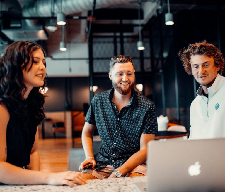 Three colleagues collaborating at a laptop in a modern office setting.