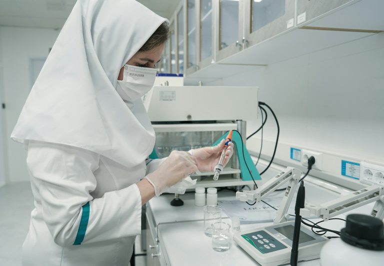 A person in a lab coat and mask preparing a syringe in a laboratory.