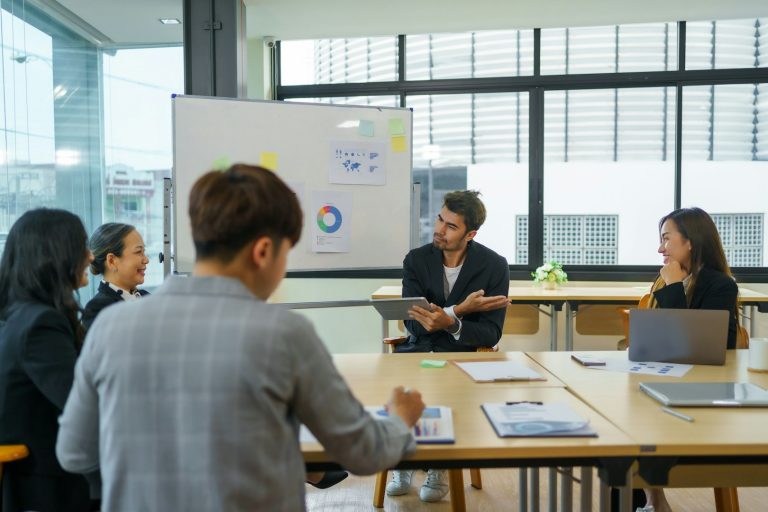 A business meeting with four people discussing around a table in a bright office.